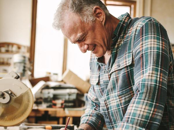 Hombre mayor escribiendo con un lápiz en un taller de carpintería