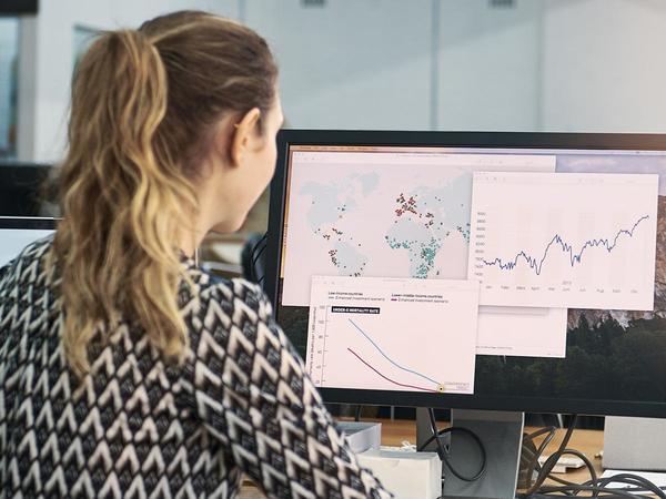 Mujer con coleta de espaldas a la imagen mirando unos gráficos en una pantalla