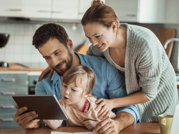 Una familia (padre, madre e hija pequeña) mirando una tablet en la cocina