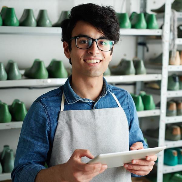 Young man with glasses and an apron holding a tablet and smiling