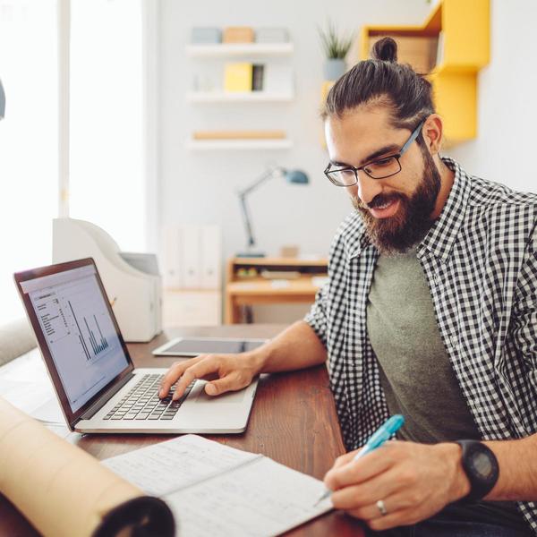 Man writing in notebook with other hand on laptop