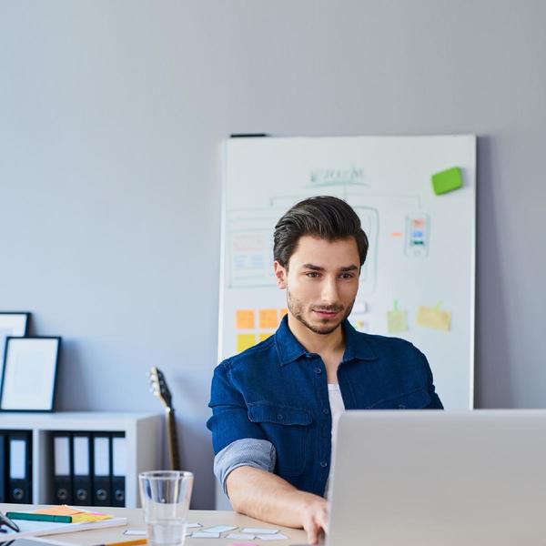 Man wearing blue shirt using laptop with a cup of water beside him