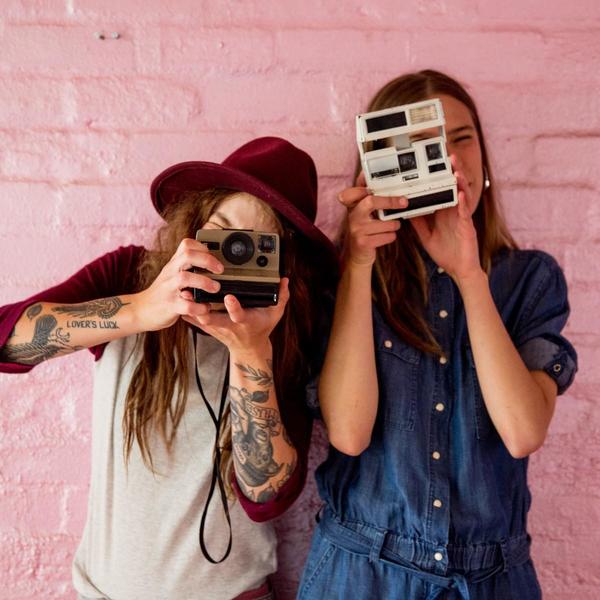 Two girls holding old cameras against pink background