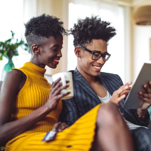 lady wearing a yellow dress while holding a mug looking at a tablet with another person