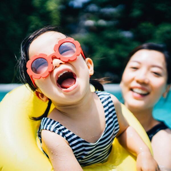 little girl on a yellow floatie with her mom at the child's back