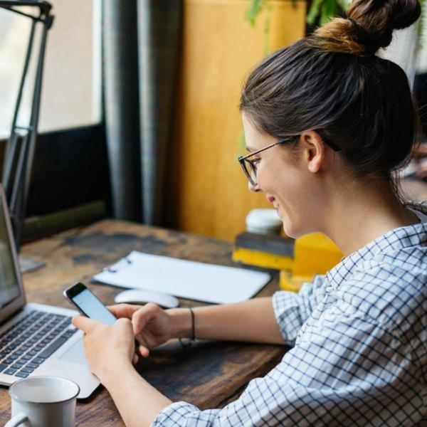 lady with glasses sitting in front of laptop and holding her phone