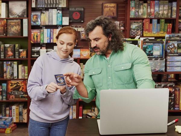 Man and woman looking at a Pokemon card in a hobby shop in front of a laptop