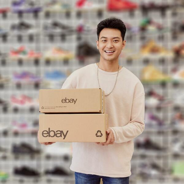Chico joven moreno sujetando dos cajas de cartón con el logo de eBay en una tienda de zapatillas deportivas