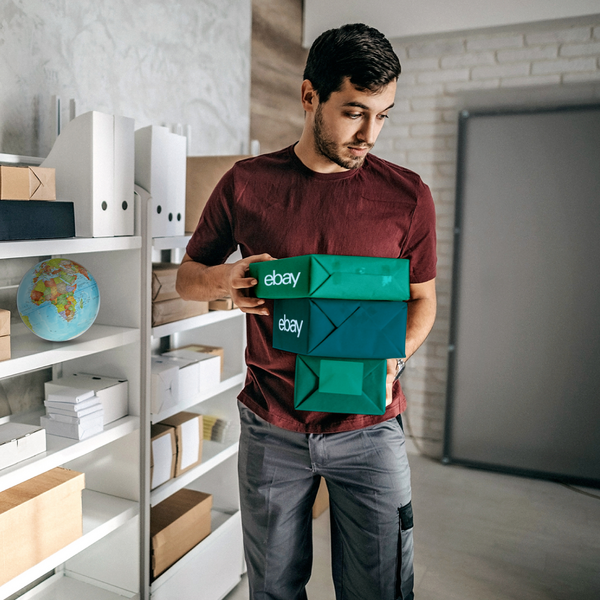 Chico joven en una oficina llevando tres paquetes envueltos en verde con el logotipo de eBay