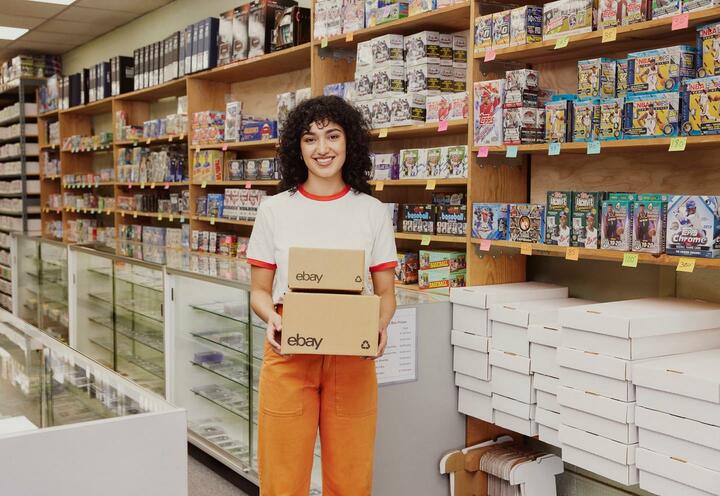 Chica joven con el pelo rizado en una tienda de juguetes sujetando dos cajas con el logo de eBay