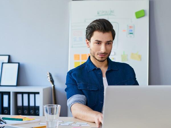 Man wearing blue shirt using laptop with a cup of water beside him