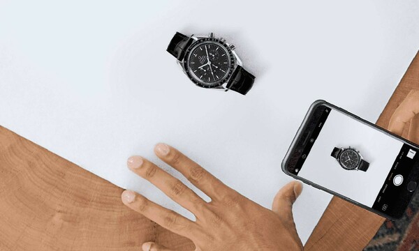 A person uses their cell phone to take a picture of a watch against a white background