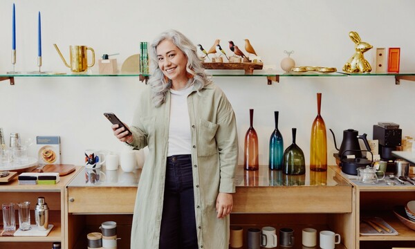 Older woman with long, grey hair holding phone and smiling at camera