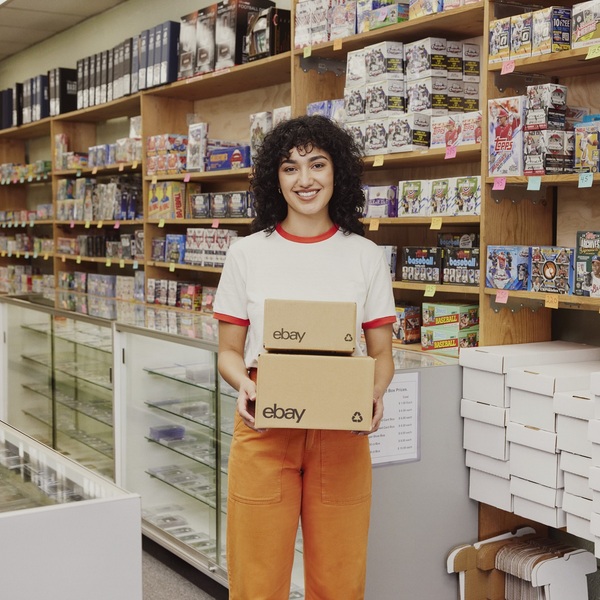 Chica joven con el pelo rizado en una tienda de juguetes sujetando dos cajas con el logo de eBay