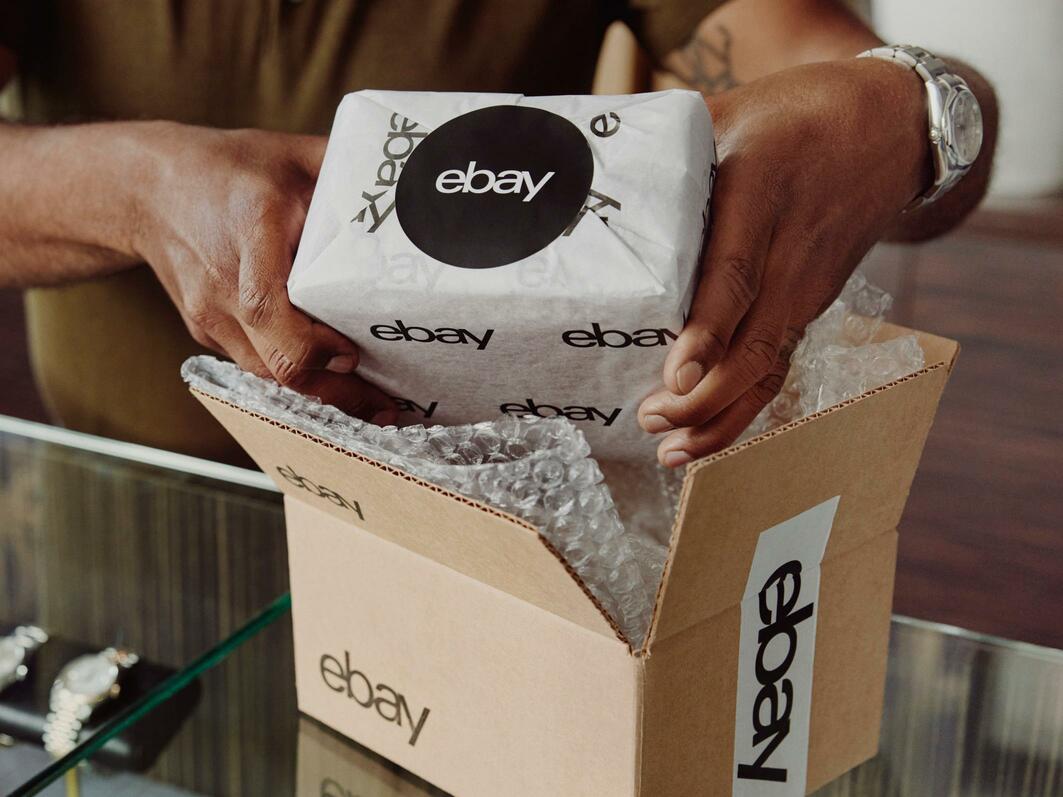 An item in eBay packaging paper being placed into an eBay labeled box.