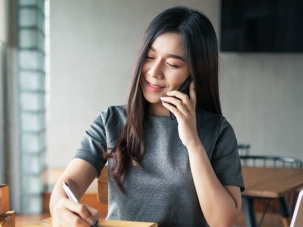 Femme au téléphone qui écrit sur un colis, un portable ouvert près d'elle