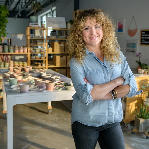 Photo d'un vendeur réel : femme aux cheveux frisés blonds qui se tient devant sa poterie les bras croisés