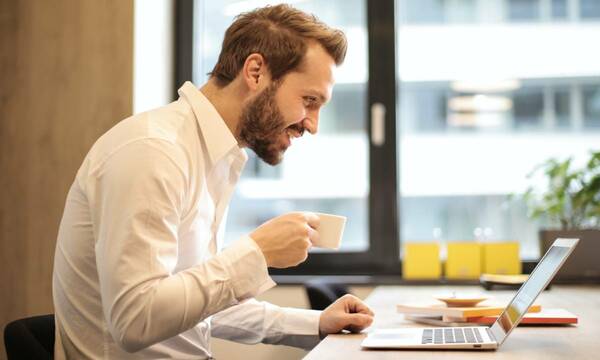 man holding cup while looking at laptop