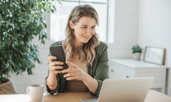 Lady holding cellphone and looking at laptop