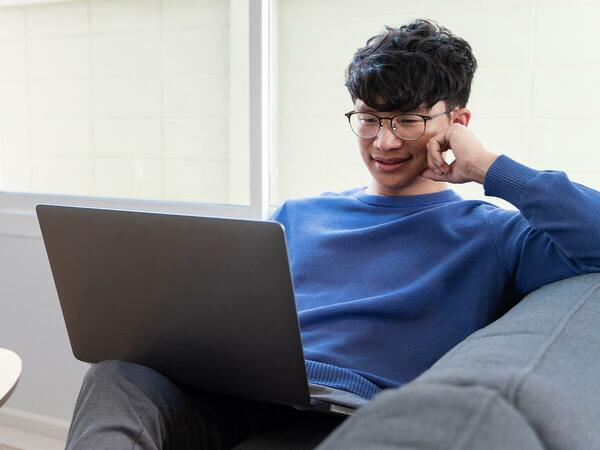 man wearing glasses while looking at laptop and sitting on a couch