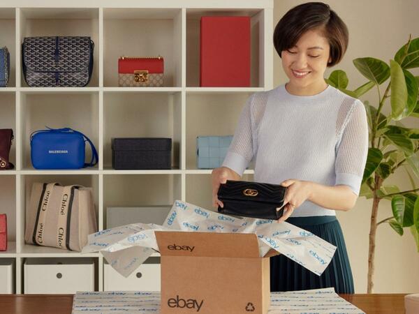 An item in eBay packaging paper being placed into an eBay labeled box. 