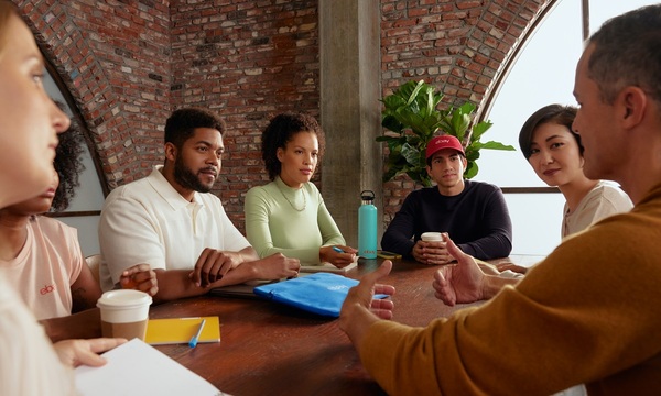 7 Menschen sitzen am Tisch und unterhalten sich