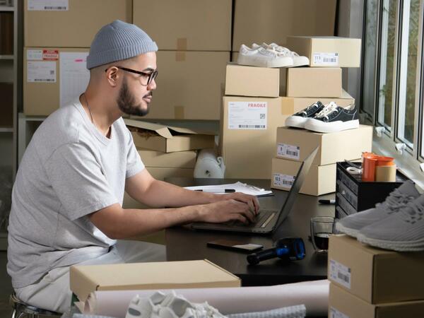 Osoba pracująca przy komputerze w pomieszczeniu z pudełkami  z butami