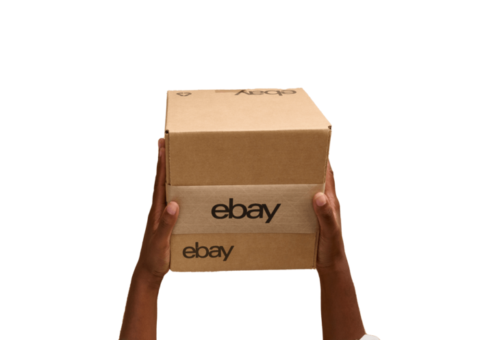 eBay seller's hands holding up a box with eBay branded tape with a green backdrop