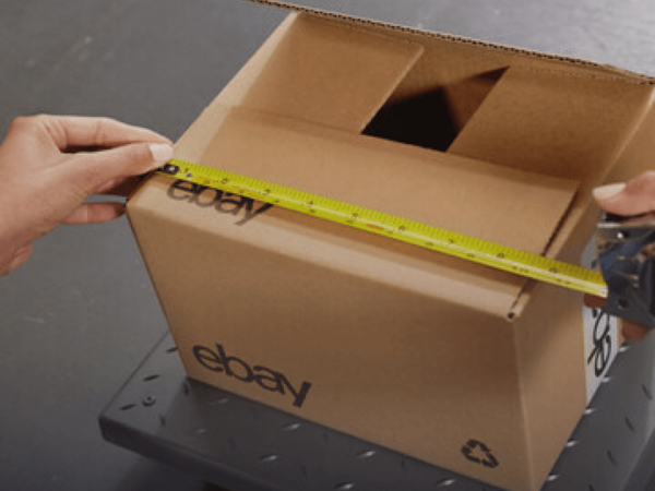 A woman using a measuring tape for an eBay shipping box on top of a weight scale.
