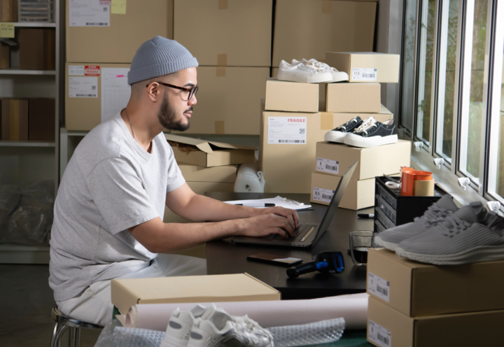 Chico con gafas y gorro sentado en mesa de trabajo con paquetes
