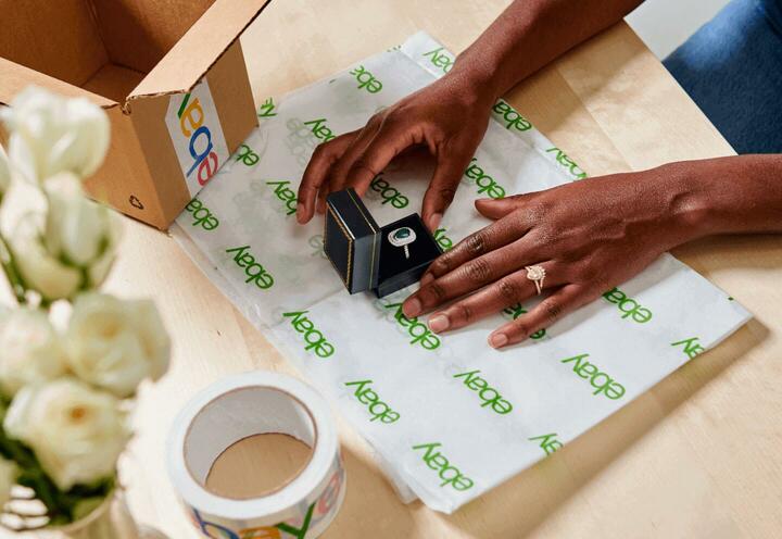 Hands wrapping a jewelry box with a ring in it, in branding white and green paper