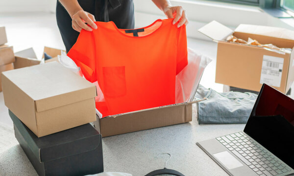 eBay buyer sitting on the floor packing an orange shirt to be returned.