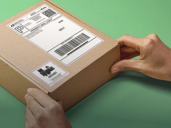 A woman’s hands holding on to a package with an eBay label and a hazmat label with a green backdrop.