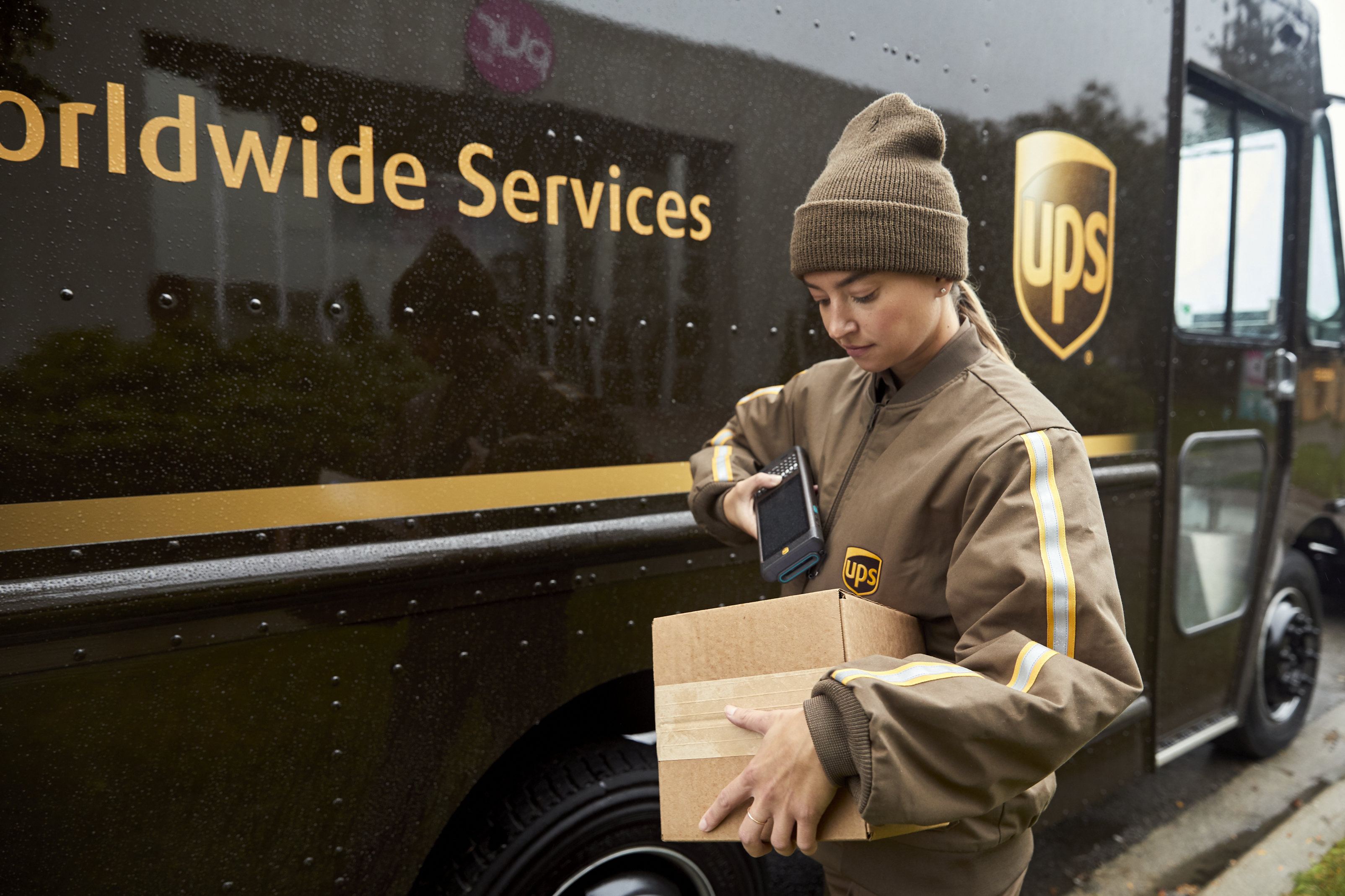 A woman scanning a package in front of a UPS truck