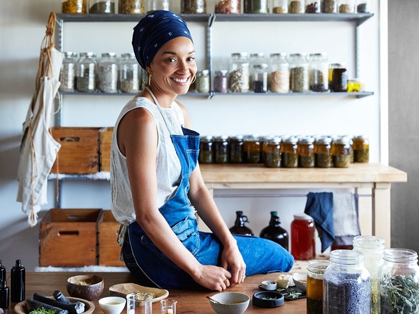 woman wearing blue apron sitting on her work bench smiling
