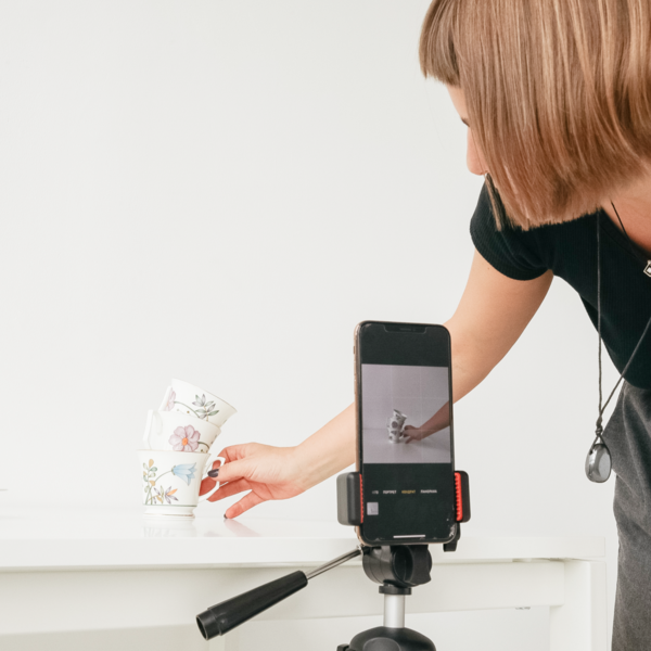 A woman using a mobile device to photograph a pair of tea cups.