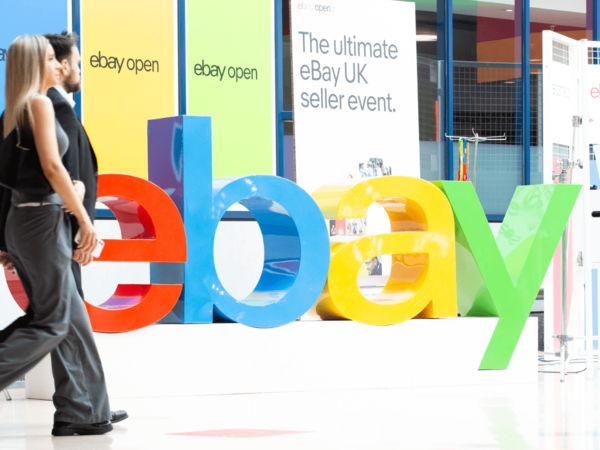 A large sign of the eBay logo with 2 people walking past.