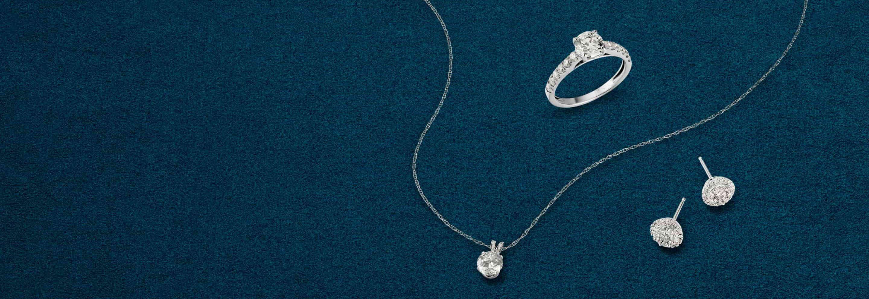 Diamond earrings, ring, and pendant with chain against a dark blue background