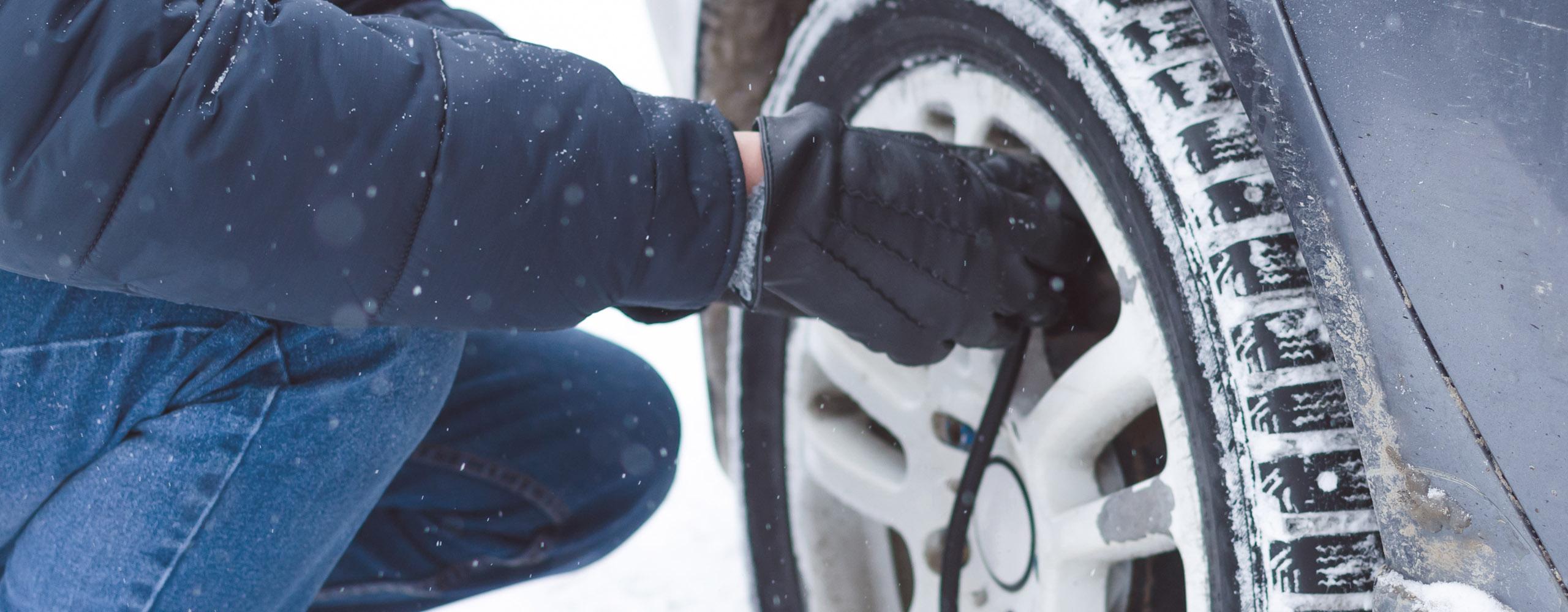 Eine Person misst den Luftdruck der Winterreifen mit einem Druckmesser.
