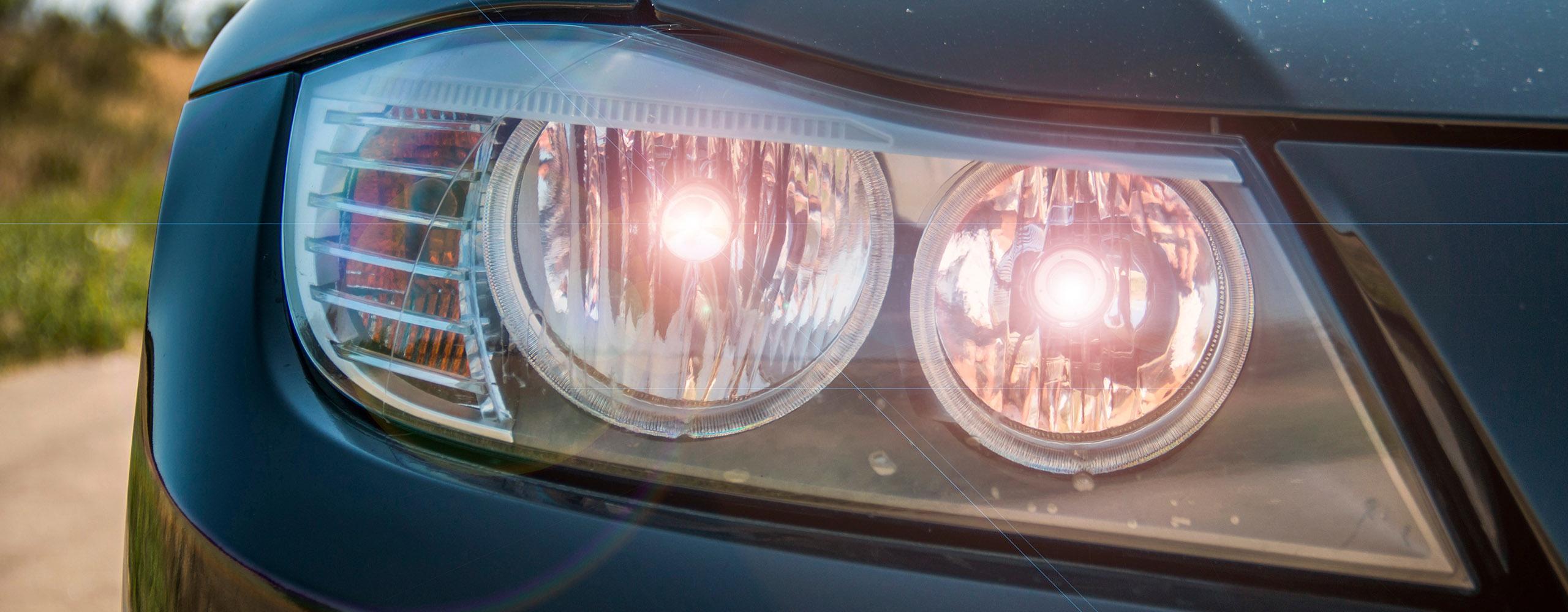 Der rechte Scheinwerfer eines schwarzen Autos mit eingeschaltetem Tagfahrlicht.