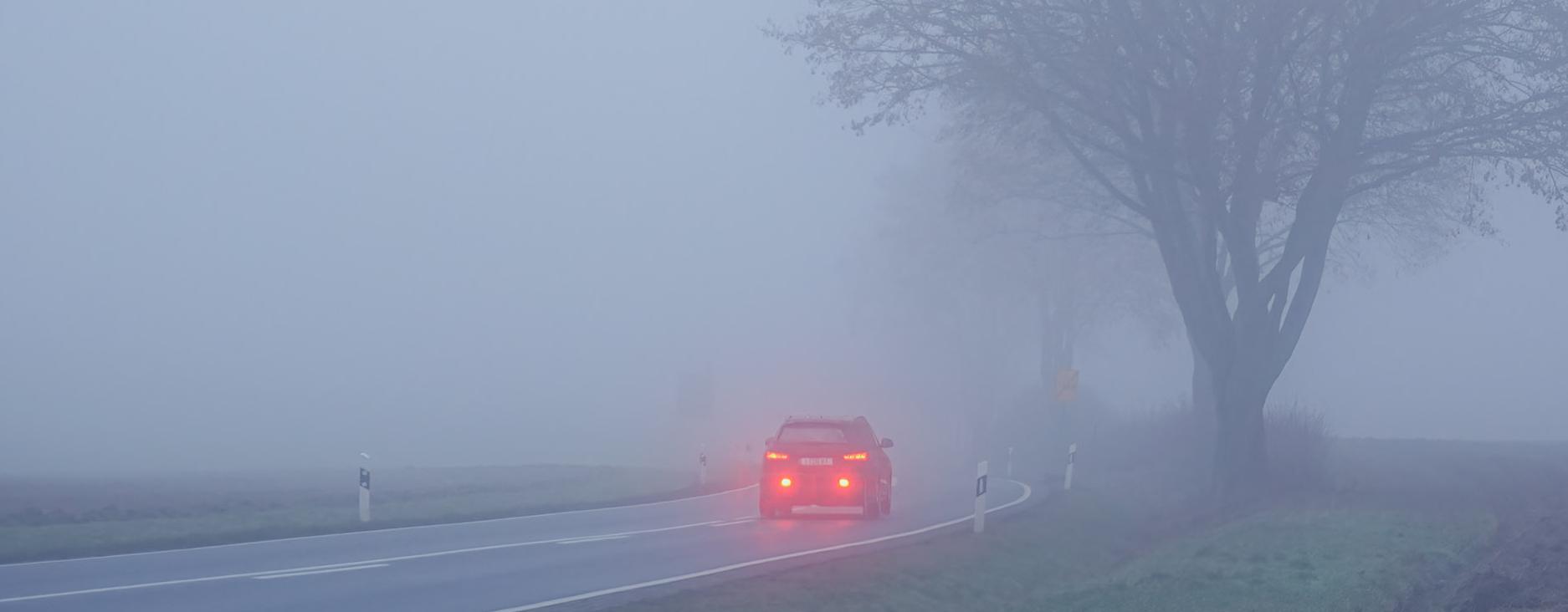 Ein Fahrzeug mit rot leuchtendem Abblendlicht fährt bei schlechten Sichtverhältnissen über eine Landstraße.