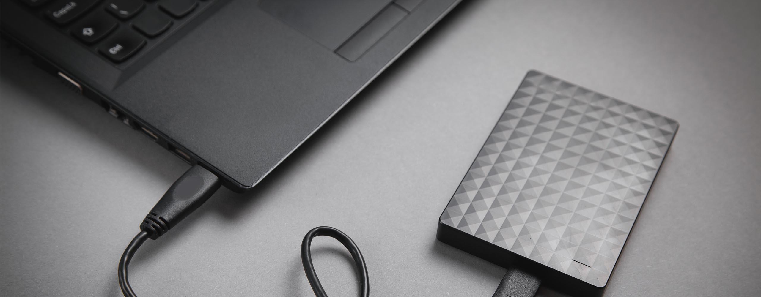Eine externe Festplatte ist über ein USB-Kabel an einen Laptop angeschlossen.