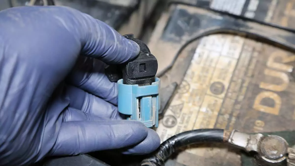 A person wearing a blue latex glove installing the replacement headlight bulb in the plug.