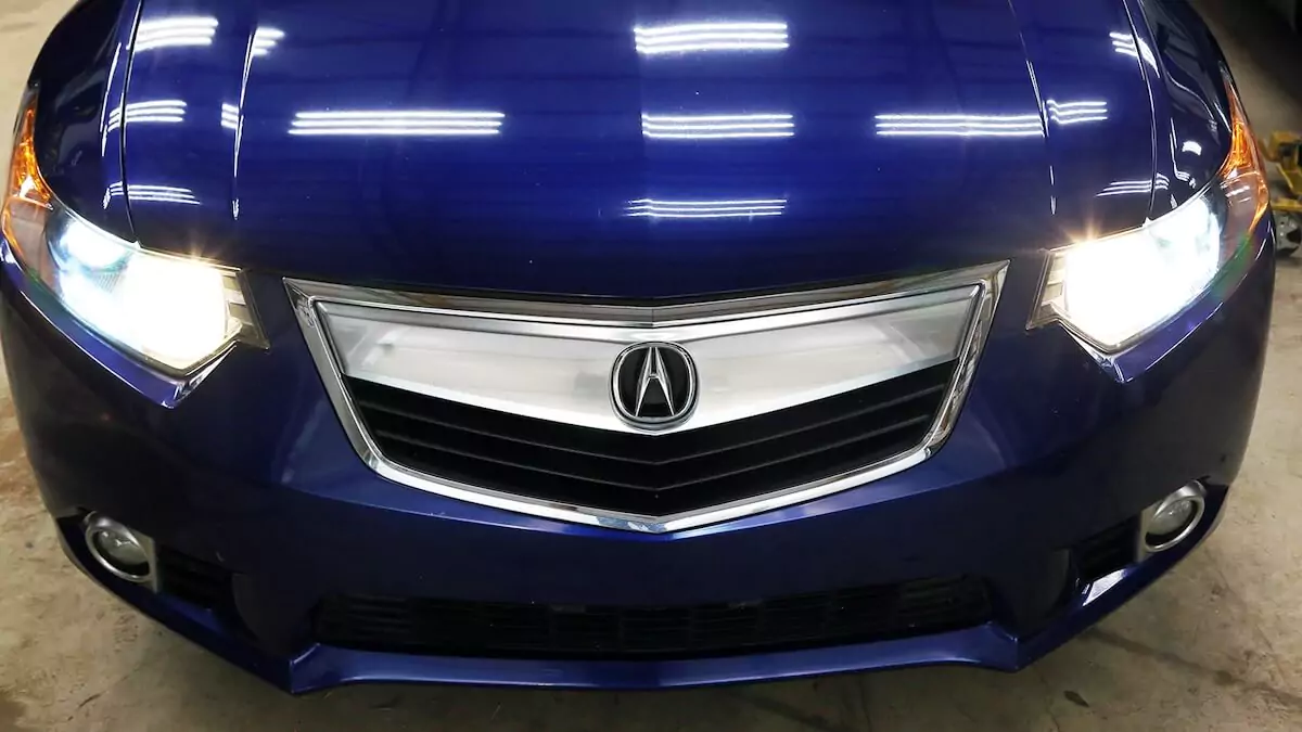 Two headlights fully illuminated in a blue Acura wagon.
