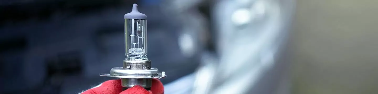 A person wearing a red and white glove holding a replacement headlight bulb.