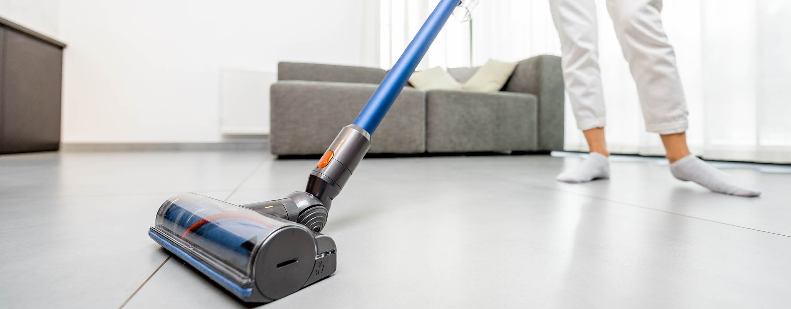 Eine Person saugt in einem Wohnzimmer mit einem kabellosen Staubsauger den Boden.