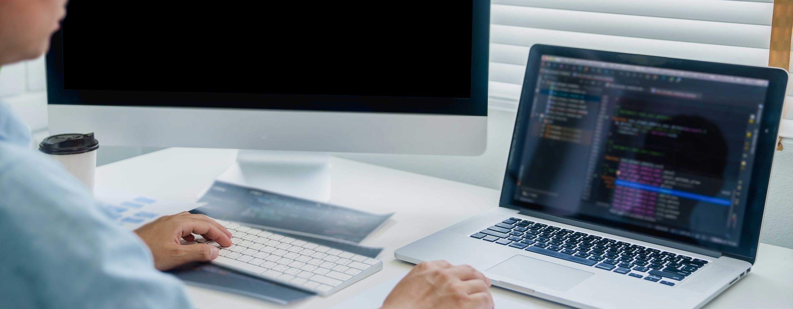 Eine Person sitzt an einem Schreibtisch, auf dem ein Laptop und ein Monitor stehen. Der Laptop erkennt den zweiten Monitor nicht, sodass letzterer schwarz bleibt.