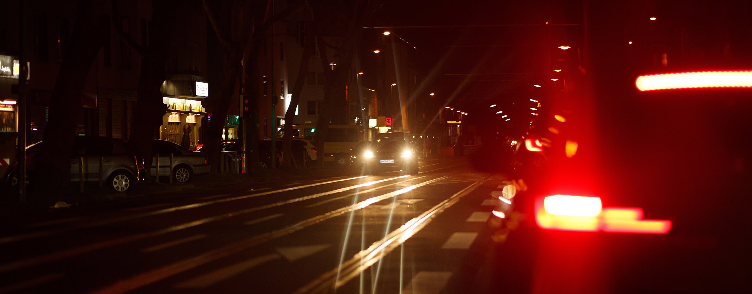 Ein bei Nacht aufleuchtendes Bremslicht auf der rechten Seite, links kommt ein Auto mit eingeschalteten Scheinwerfern entgegen.