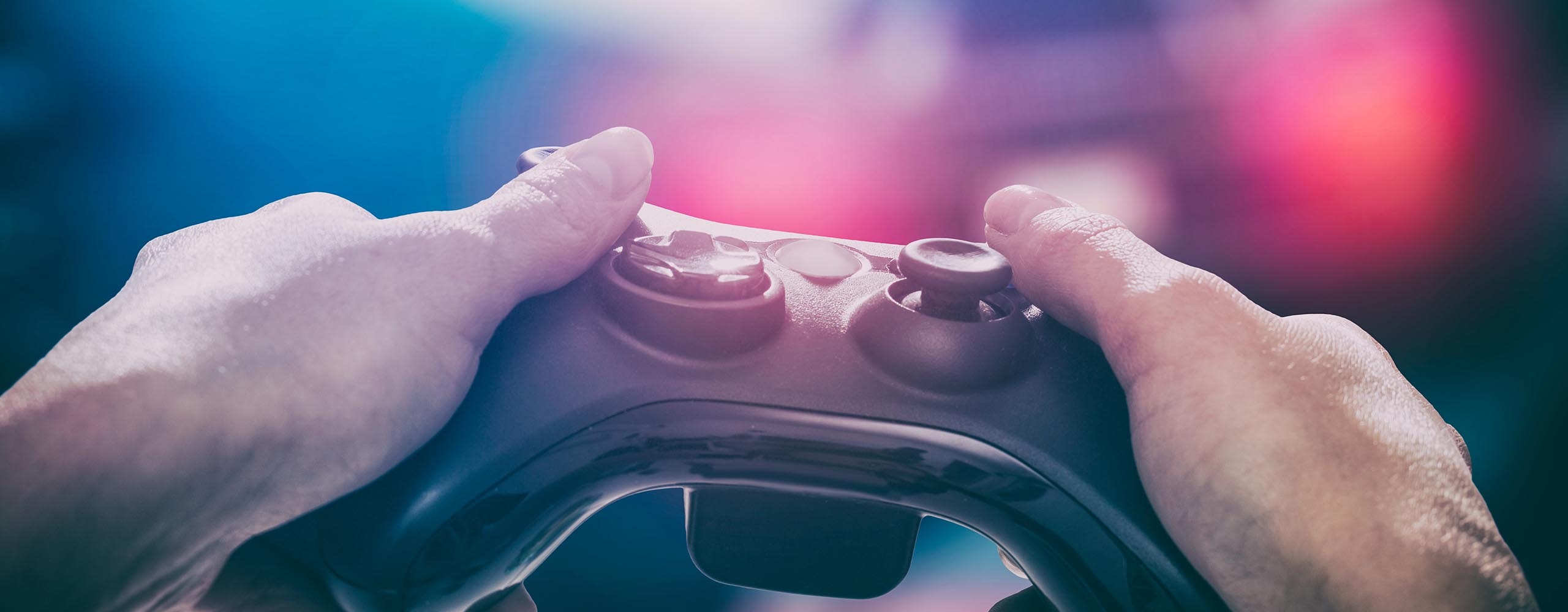 Nahaufnahme von zwei Händen, die einen Gaming-Controller halten. Im Hintergrund sieht man einen Monitor, auf dem ein Auto gesteuert wird.