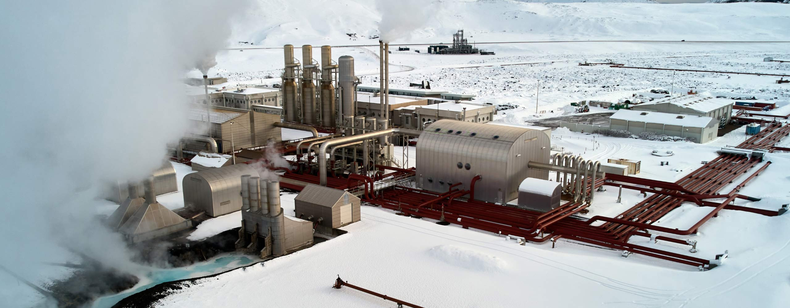 Ein Geothermiekraftwerk mit dampfenden Türmen, Rohren und Gebäuden in einer schneebedeckten Landschaft